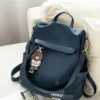 Navy blue backpack purse placed on sofa with cute charm keychain and adjustable straps