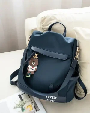 Navy blue backpack purse placed on sofa with cute charm keychain and adjustable straps