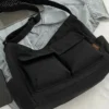 Trendy black oversized messenger bag placed beside laptop and denim outfit