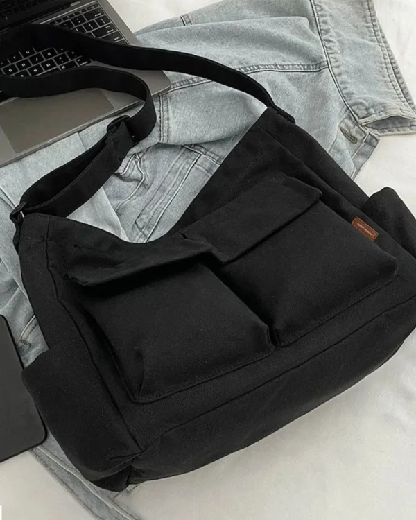 Trendy black oversized messenger bag placed beside laptop and denim outfit