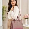 Elegant pink structured handbag for women carried by a model, featuring dual top handles, detachable shoulder strap, textured finish, and gold-tone hardware.