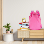Pink kids backpack with padded back support placed beside books on wooden table