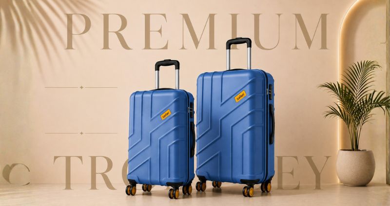 Premium blue hard-shell trolley luggage set displayed in a luxury beige studio setting with elegant oversized background typography, spinner wheels, and telescopic handles.